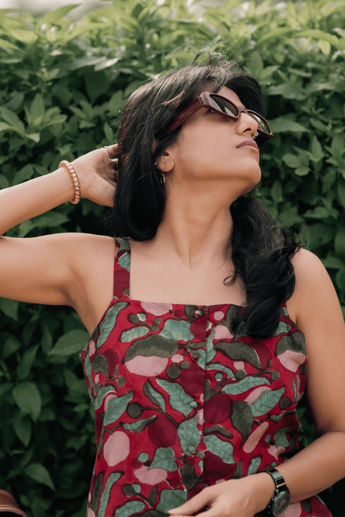 Woman wearing a red floral dress with sunglasses against a green leafy background