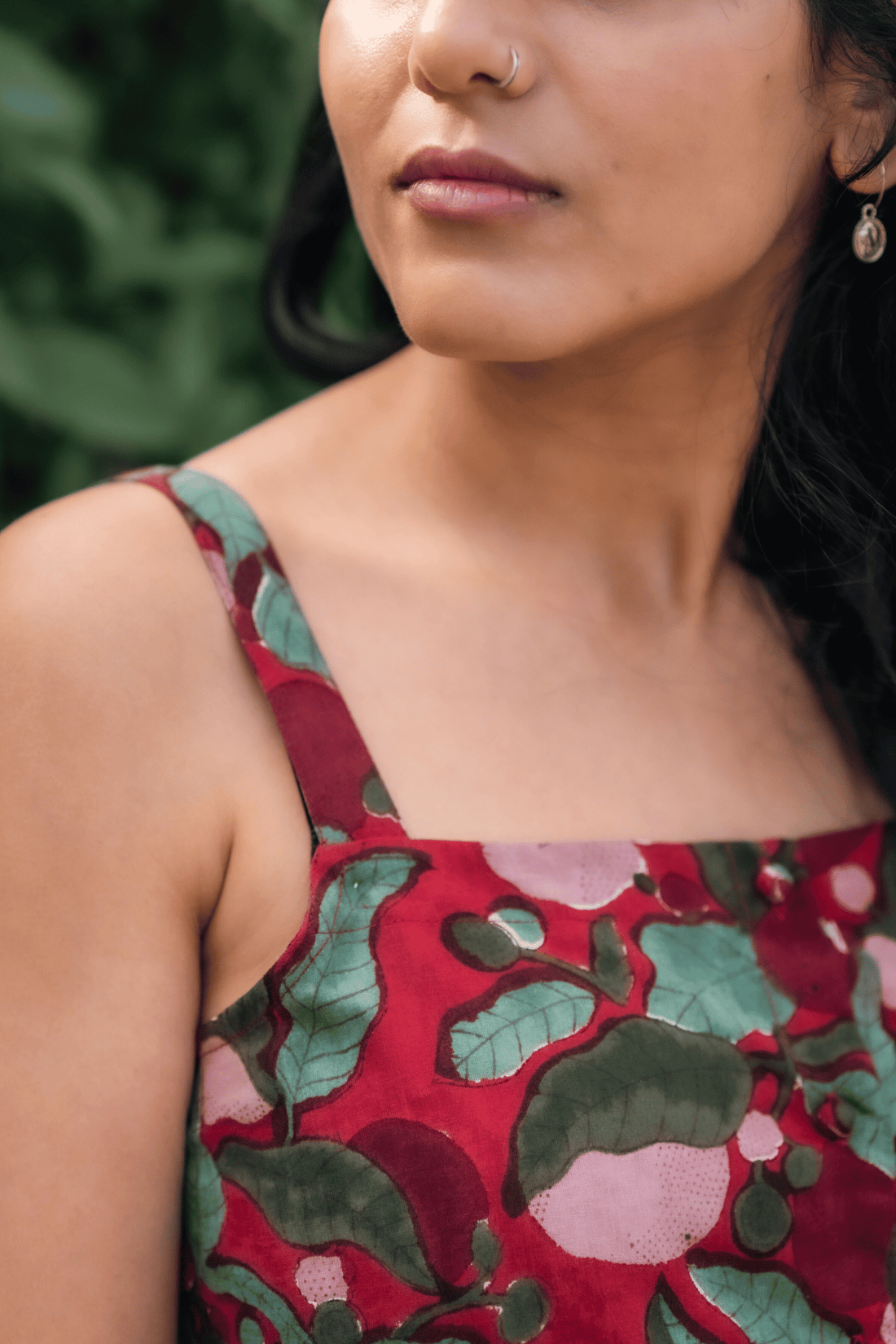 Woman wearing a red floral dress with sunglasses against a green leafy background