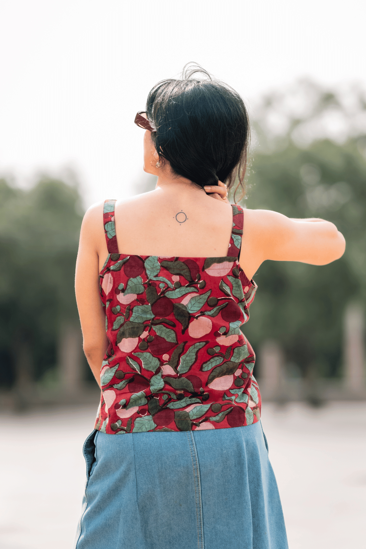 Person wearing a red floral tank top with a blurred natural background