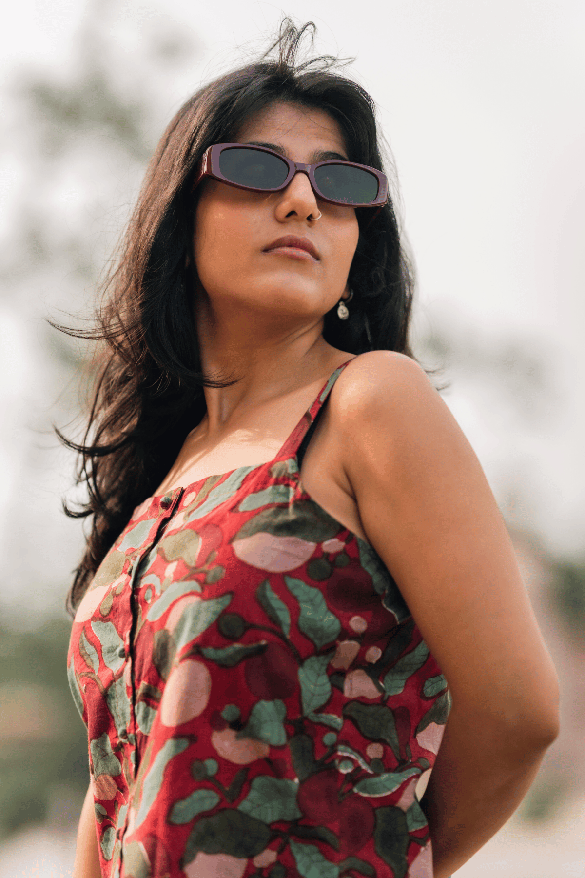 Woman wearing sunglasses and a red floral dress with a blurred background