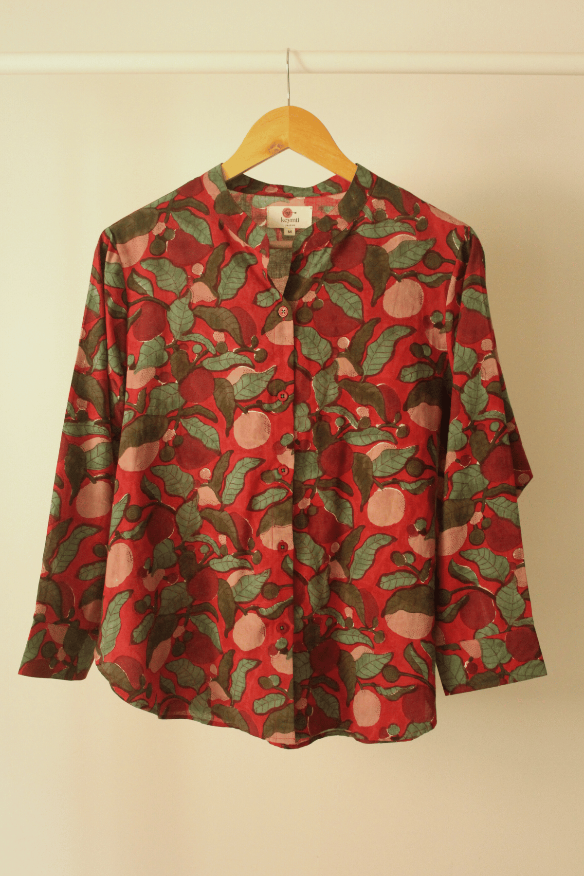 Red shirt with green leaf pattern on a hanger against a beige wall